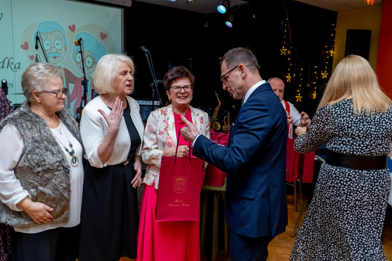Mężczyzna wręcza torebkę prezentową grupie kobiet.