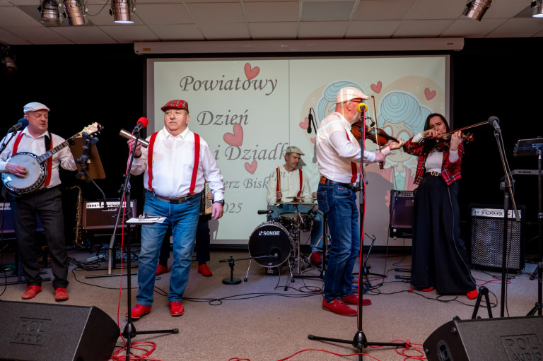 Grupa ludzi występuje na scenie grając na instrumentach.