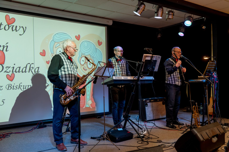 Trzech mężczyzn występuje na scenie grając na instrumentach.