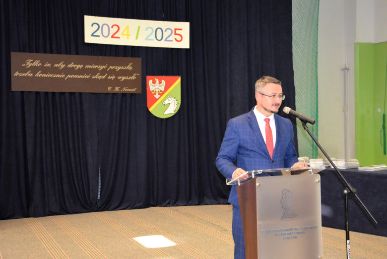 Mężczyzna w granatowym garniturze przemawia do mikrofonu.