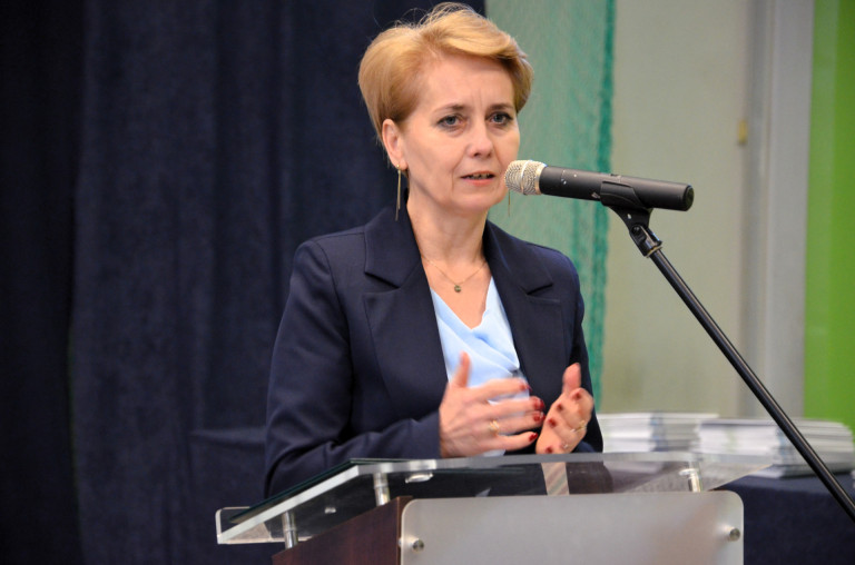 Kobieta w granatowej marynarce przemawia do mikrofonu.