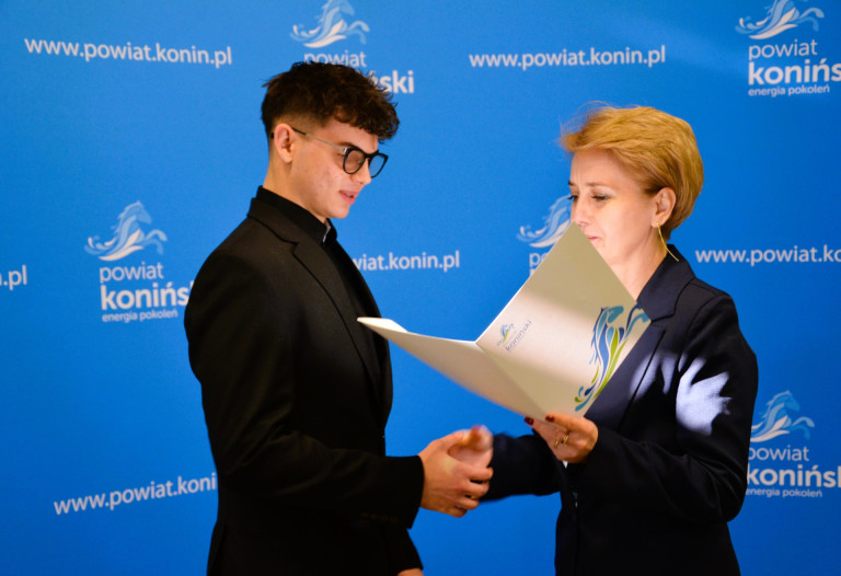 Kobieta wręcza nagrodę mężczyźnie w czarnym garniturze.