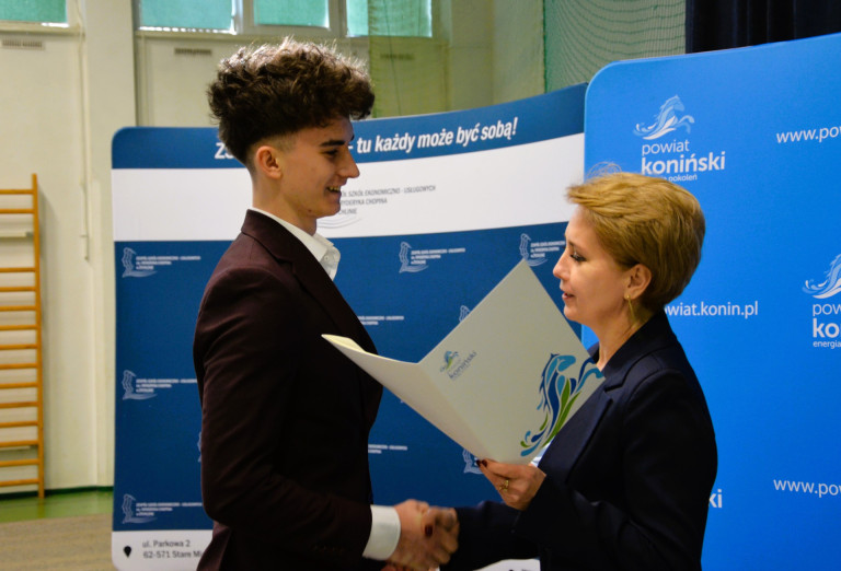 Kobieta wręcza nagrodę mężczyźnie w garniturze.