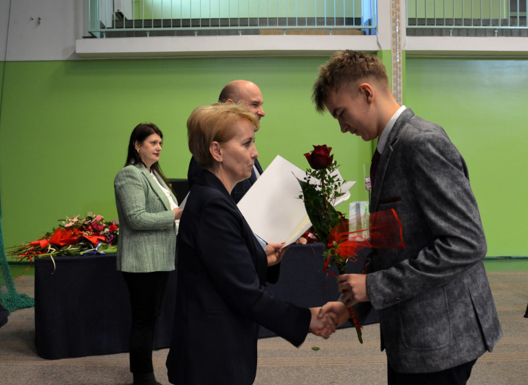 Kobieta wręcza nagrodę mężczyźnie w garniturze.