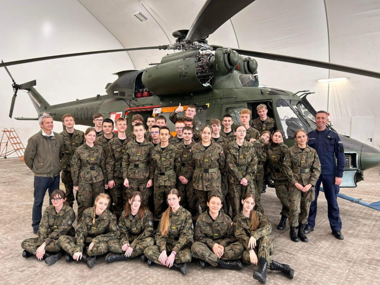 Grupa mężczyzn i kobiet w mundurach przed helikopterem.
