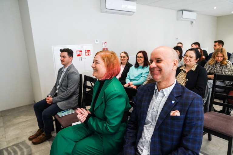 Grupa ludzi siedzi na krzesłach w jasnej sali.