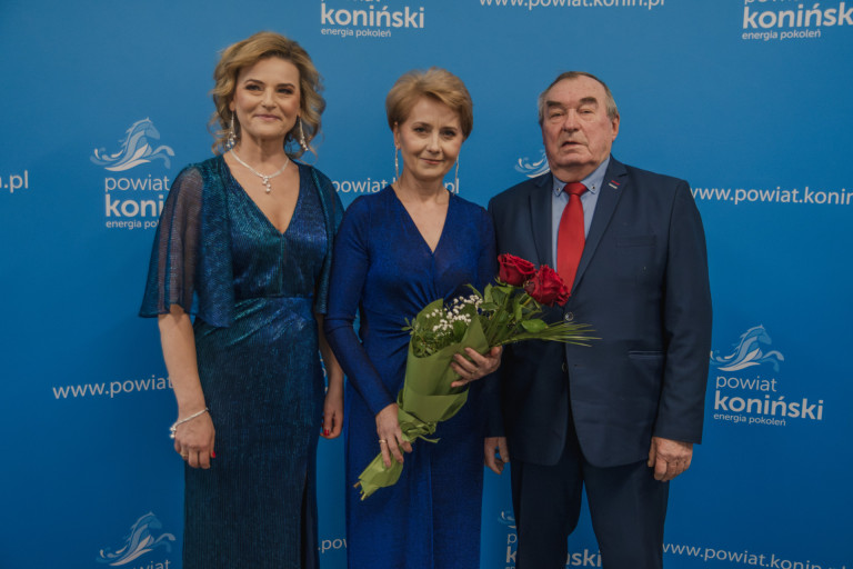 Dwie kobiety stoją obok mężczyzny. Jedna z kobiet trzyma bukiet kwiatów.