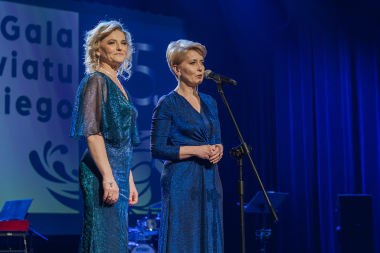 Dwie kobiety w niebieskich sukienkach stoją na scenie.