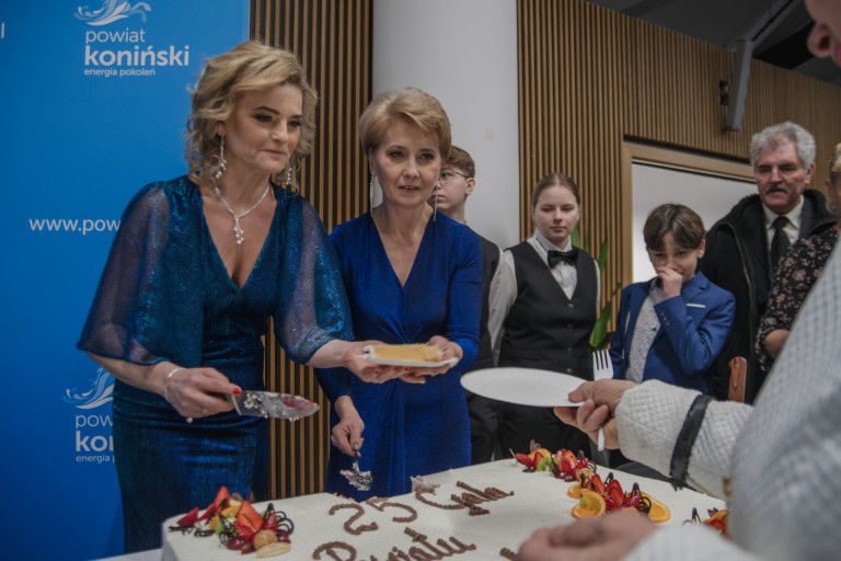 Dwie kobiety w niebieskich sukienkach kroją tort.
