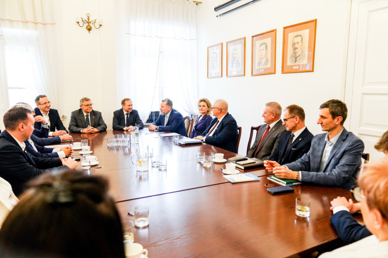 Grupa ludzi siedzi przy stole w sali konferencyjnej.