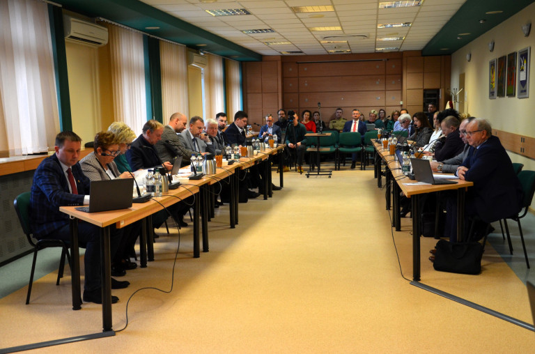 Grupa ludzi siedzi przy stołach w sali konferencyjnej.