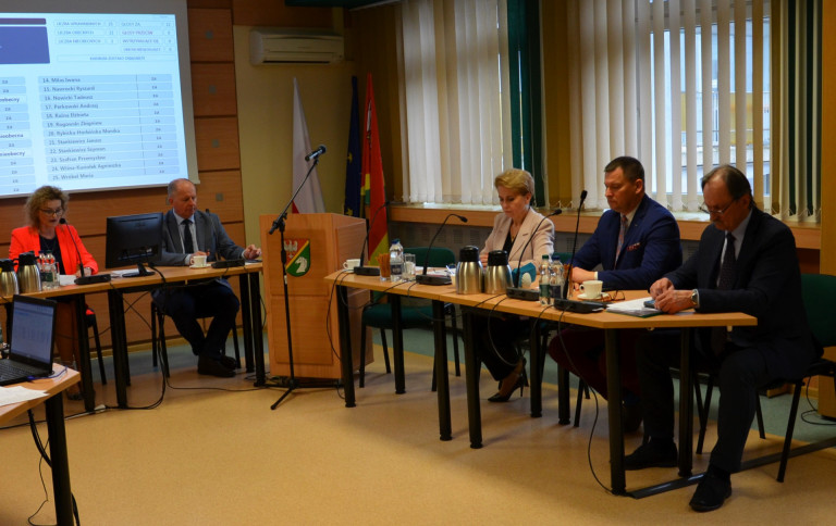 Grupa ludzi siedzi przy stole w sali konferencyjnej.