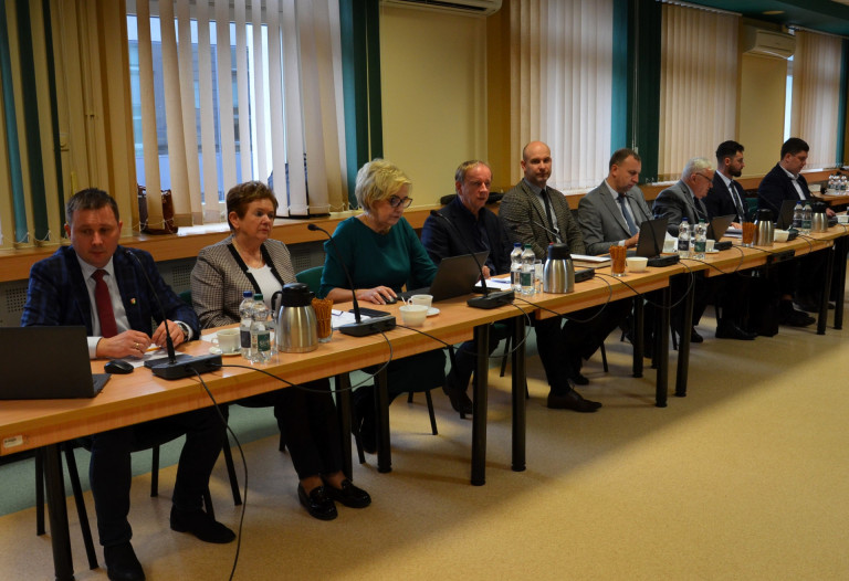 Grupa ludzi siedzi przy stole w sali konferencyjnej.