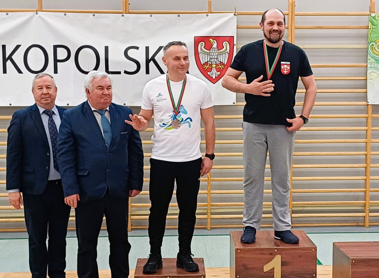 Dwóch mężczyzn stoi na podium. Z lewej strony podium stoi dwóch mężczyzn.