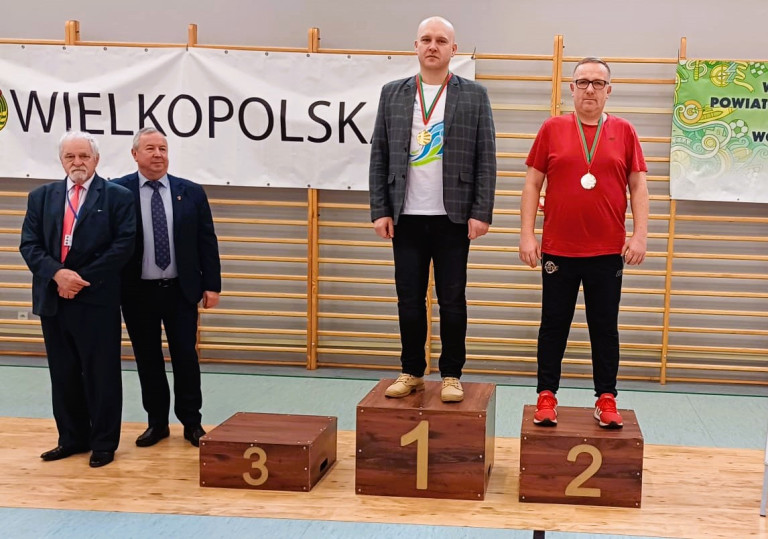 Dwóch mężczyzn stoi na podium. Obaj mają medal na szyi.