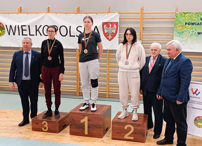 Trzy kobiety stoją na podium. Każda z nich ma medal na szyi.