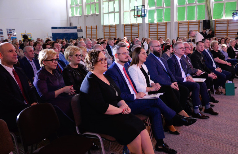 Liczna widownia siedzi w sali gimnastycznej.