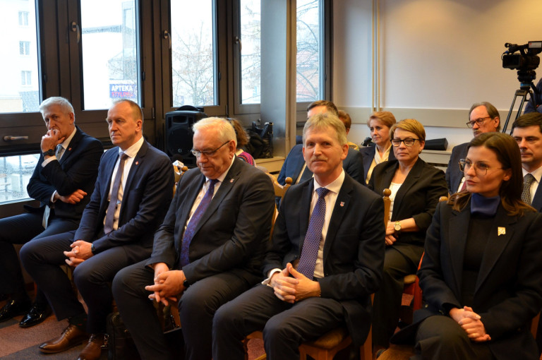 Kilkoro mężczyzn oraz kobiet siedzący w sali.