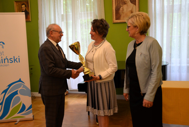 Dwie kobiety i mężczyzna. Mężczyzna wręcza kobiecie puchar.